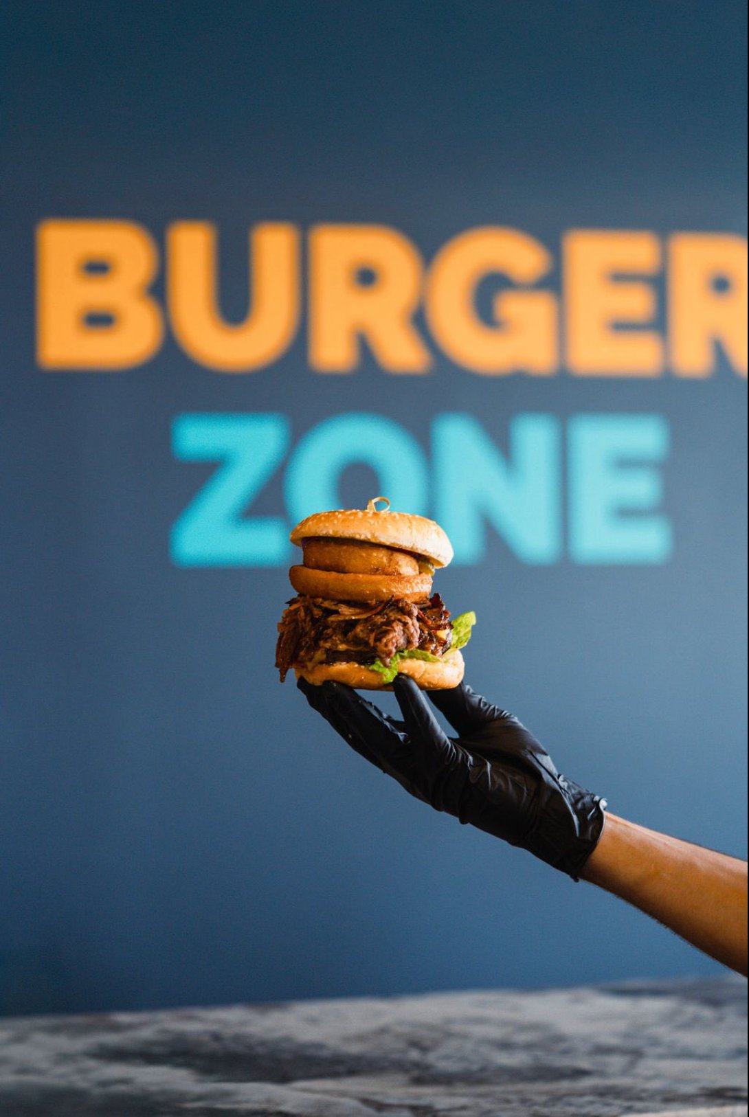 Chef holding burger — Burger Zone sign